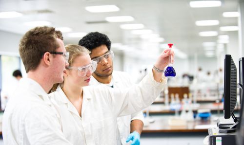 Three researchers examining a sample in a laboratory